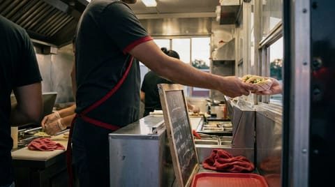 A food truck worker handing tacos out of the service window at dusk